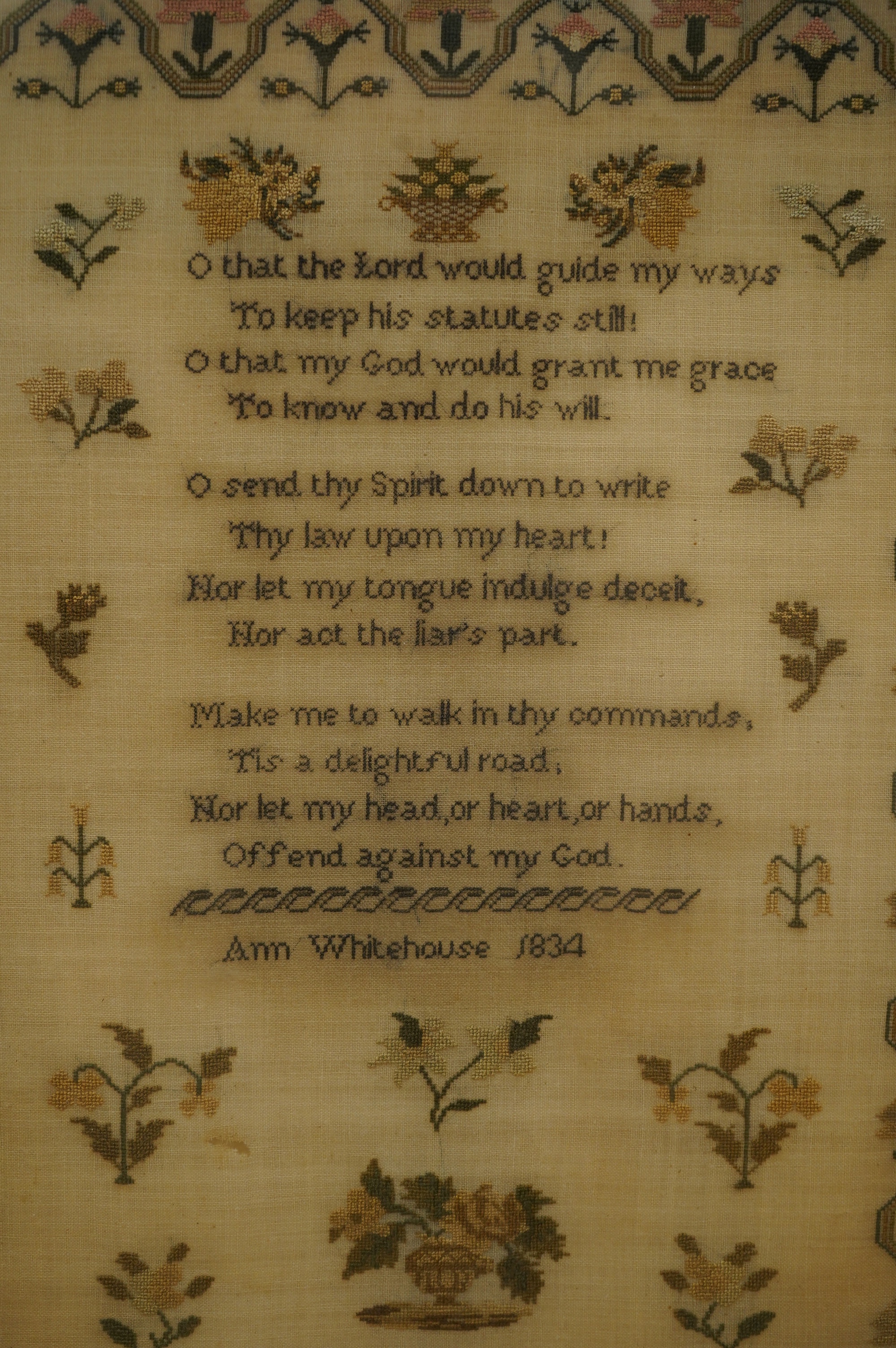 A wide mahogany framed sampler by Ann Whitehouse dated 1834, worked in coloured silks on a fine linen ground, in small stitches, bordered with a geometric stylistic vining pattern, set with a central verse, above her nam